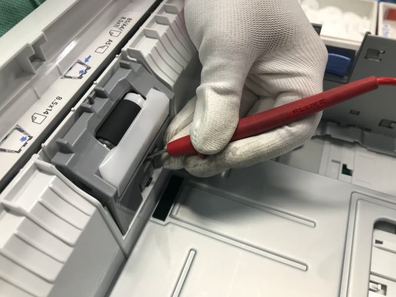 Manos con guante revisando el rodillo de papel de una impresora abierta